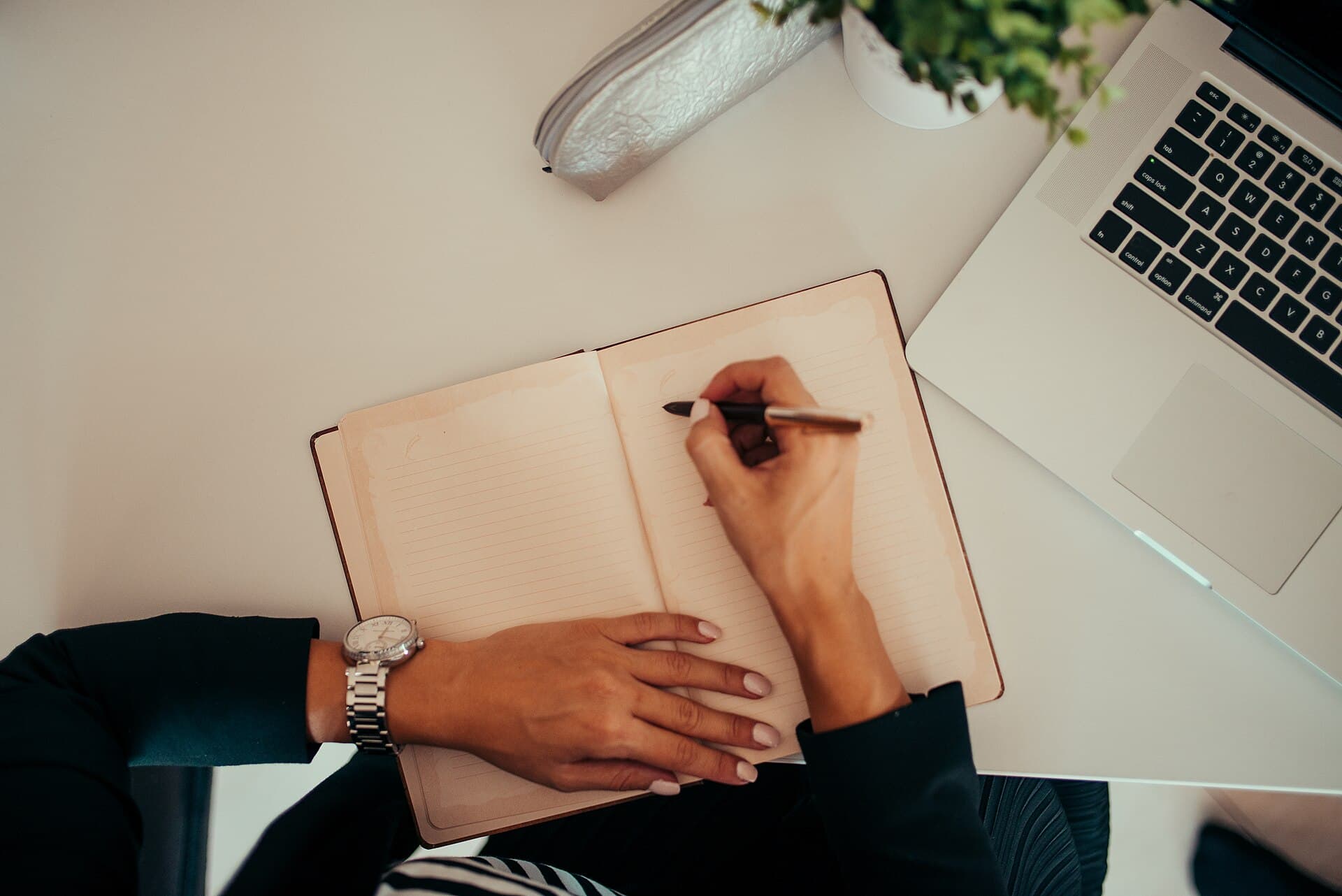 Personne qui écrit dans un carnet à côté d'un ordinateur portable sur un bureau